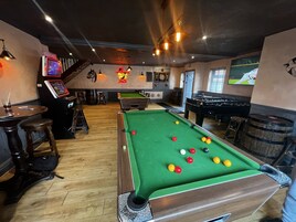 Una sala de billar con mesa de pool, taburetes y dardo.