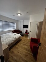 Un dormitorio con cama, televisor, armario y zona de estar con sillones.