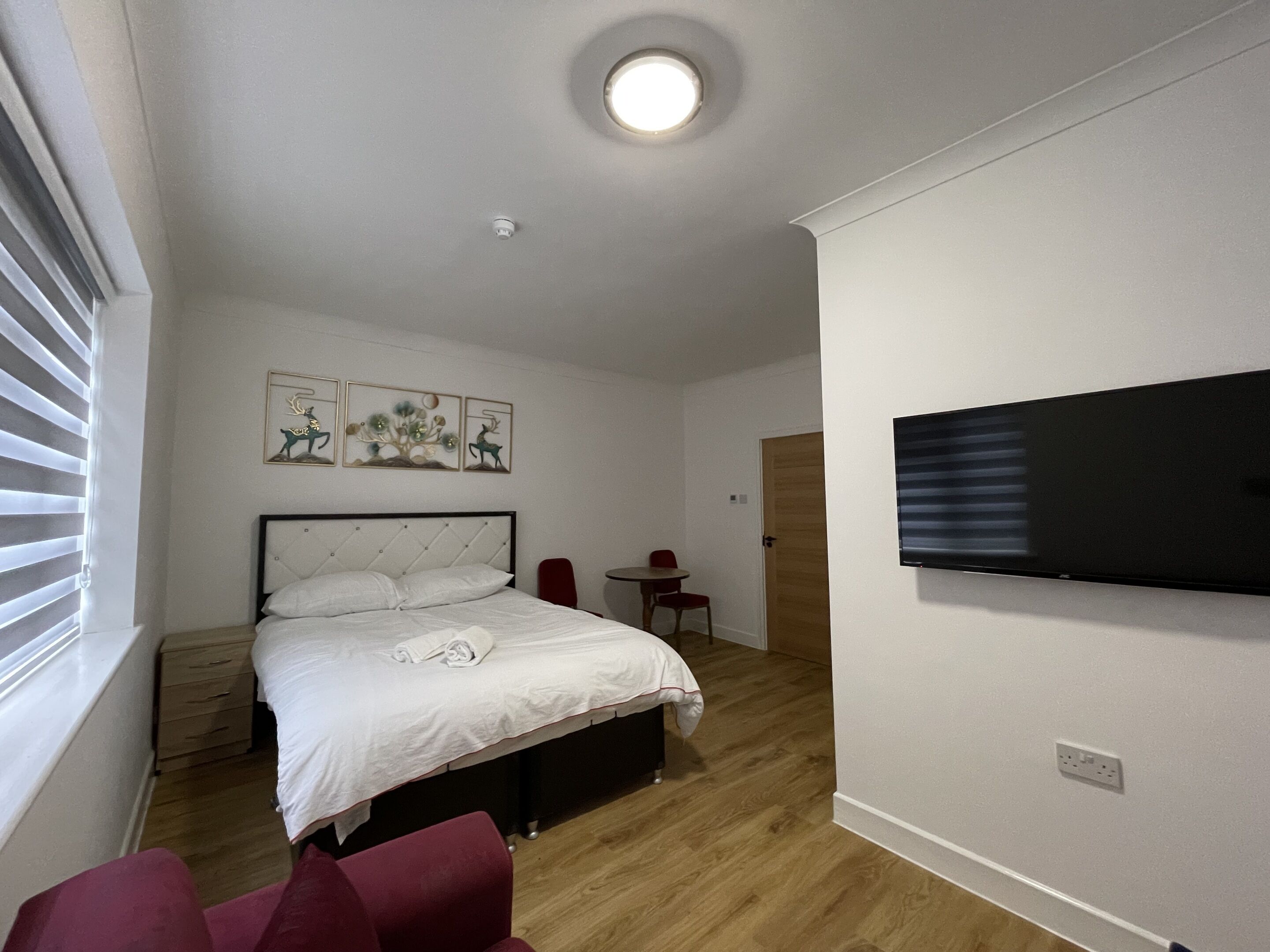 A bedroom with a bed, a TV, a small table, and a chair.