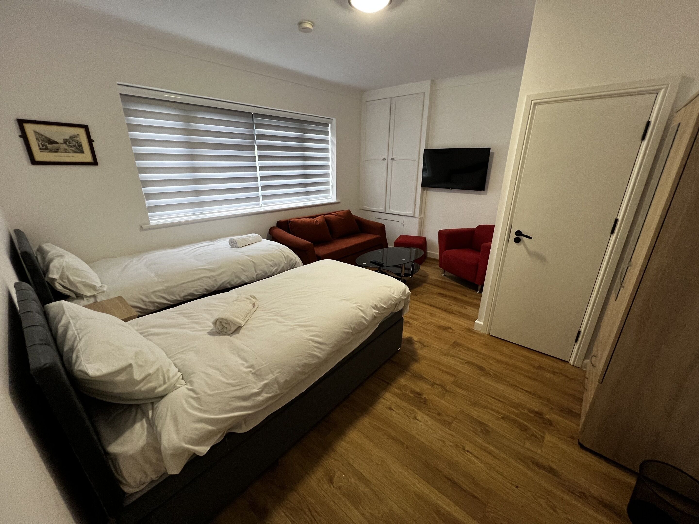 A bedroom with two beds, a TV, a sofa, and a door.
