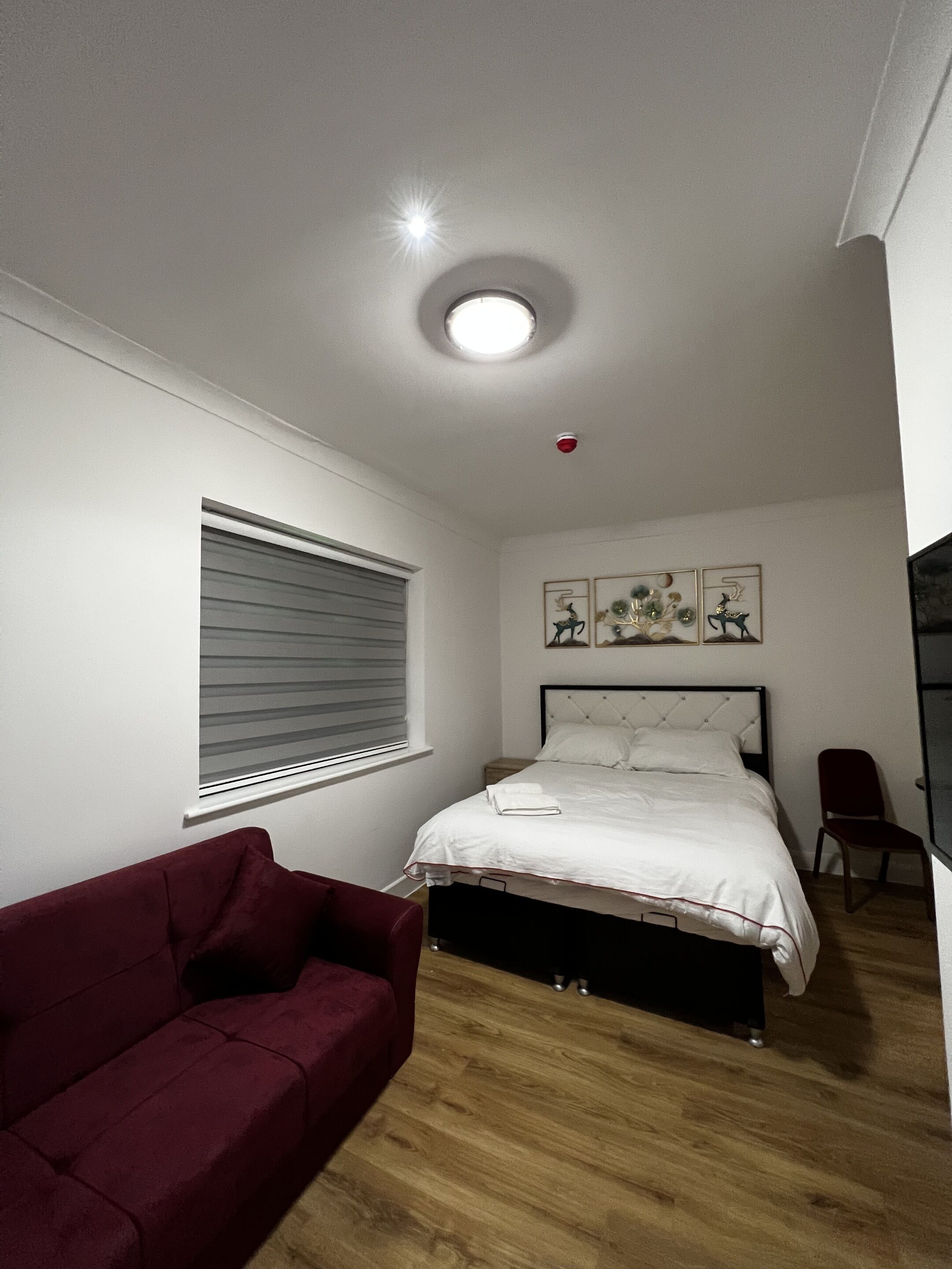 Quarto com uma cama, um sofá vermelho, uma janela com persianas e uma luminária no teto.