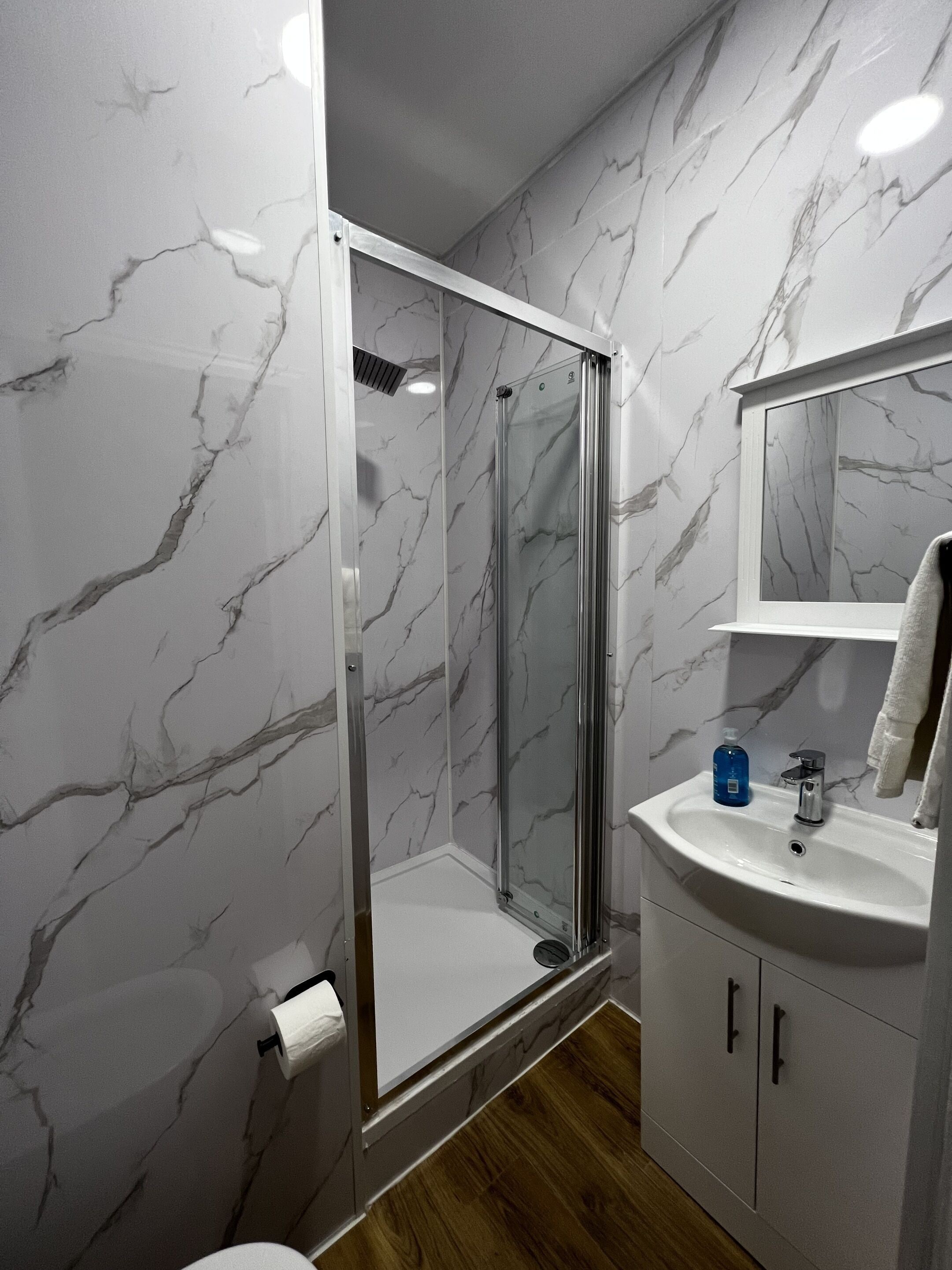Een badkamer met een glazen douchecabine, een wastafel met spiegel en wanden met een marmerprint.