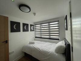 Un dormitorio con cama, ventana con persianas, lámpara de pared y tres cuadros con imágenes de la luna.