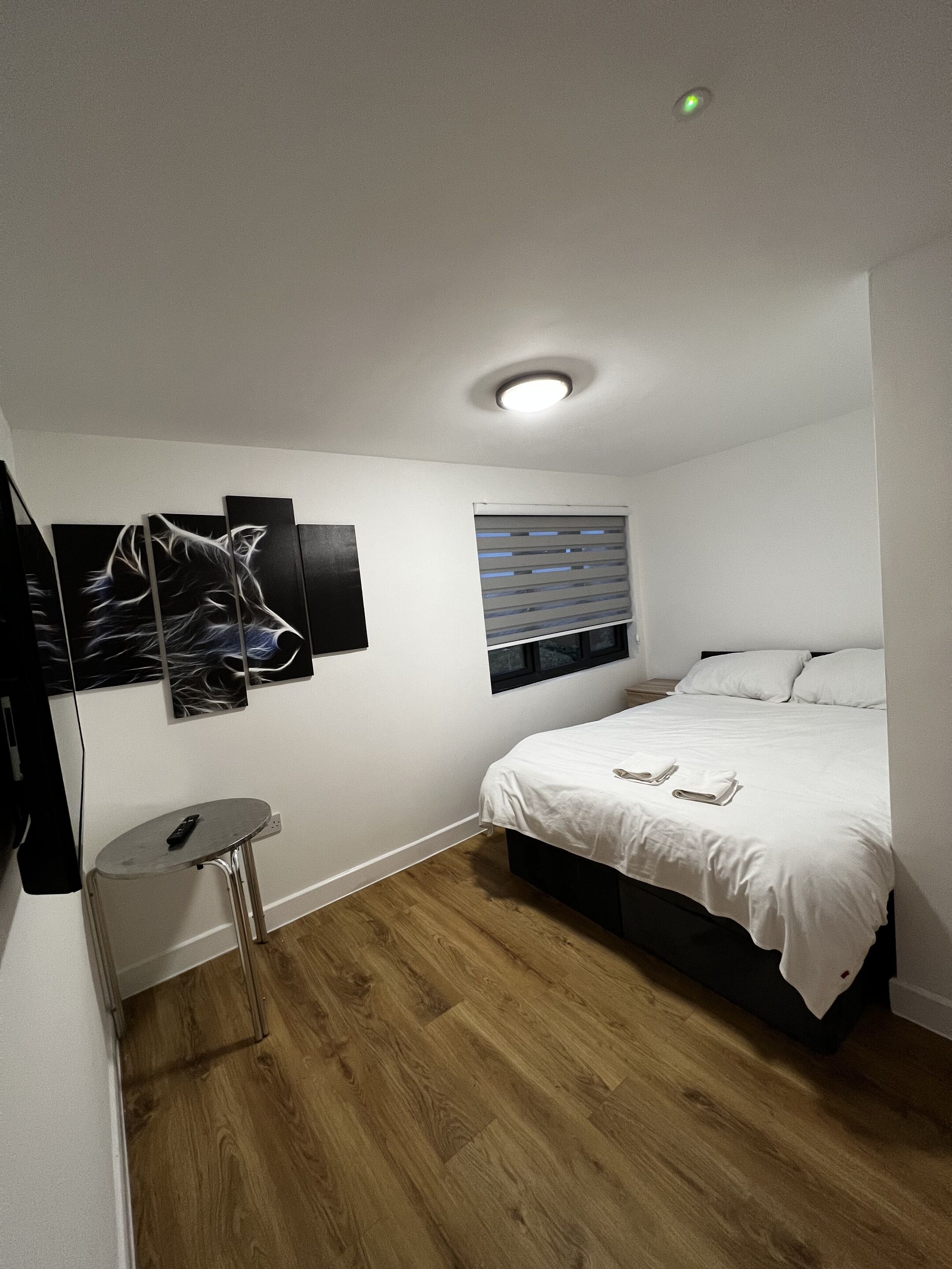 A bedroom with a bed, a small table, a wall-mounted TV, and artwork.