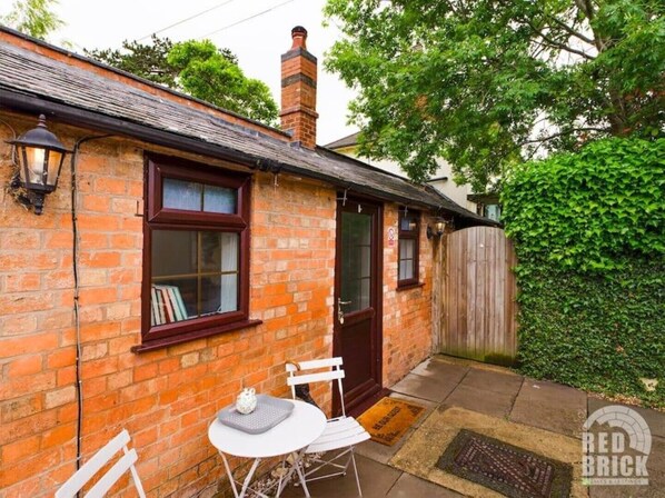 A brick house with a small patio, a white chair, a table, and a wooden fence.