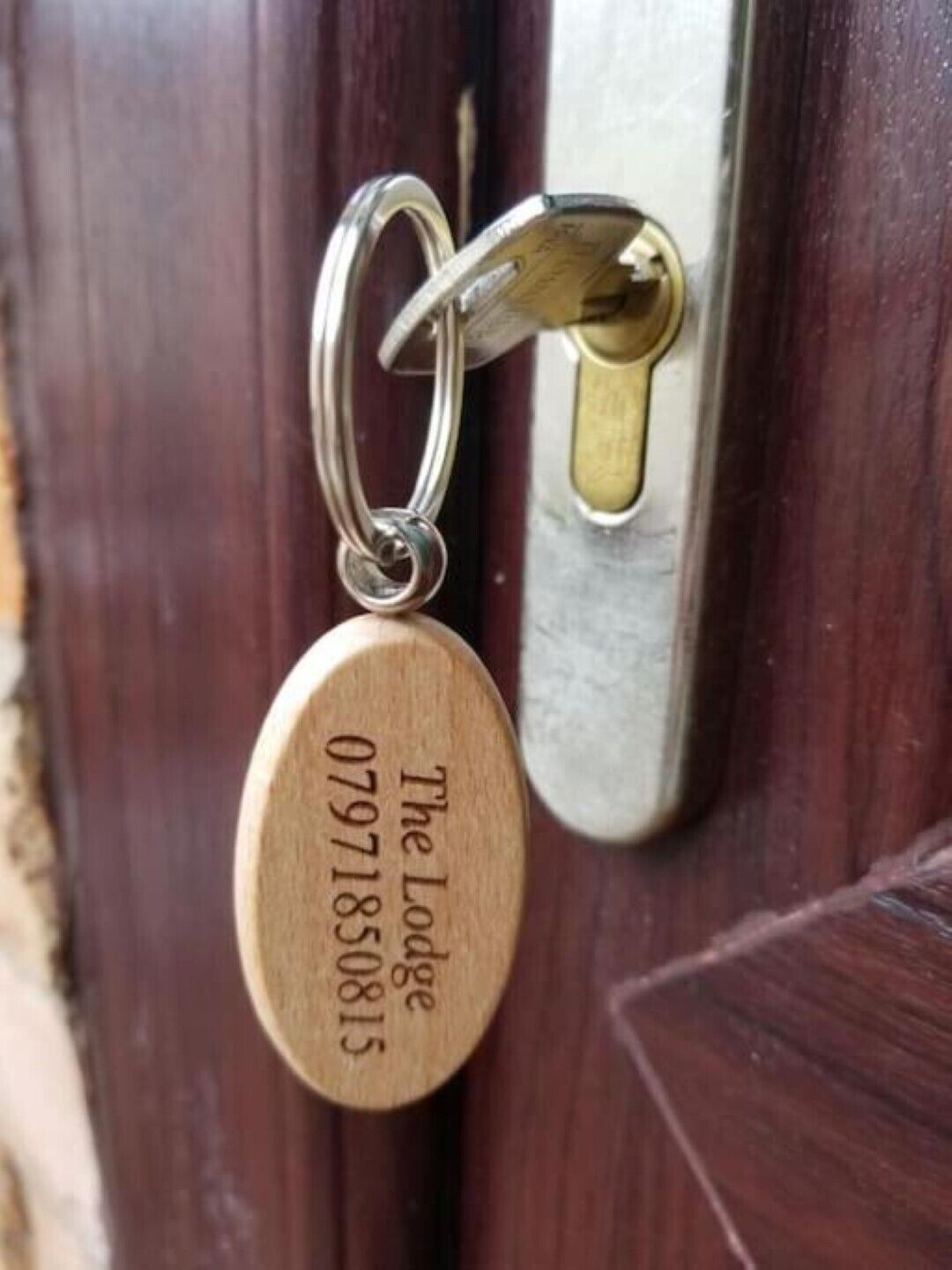 A wooden key with engraved text "The Lodge 07971850815" attached to a keyring.
