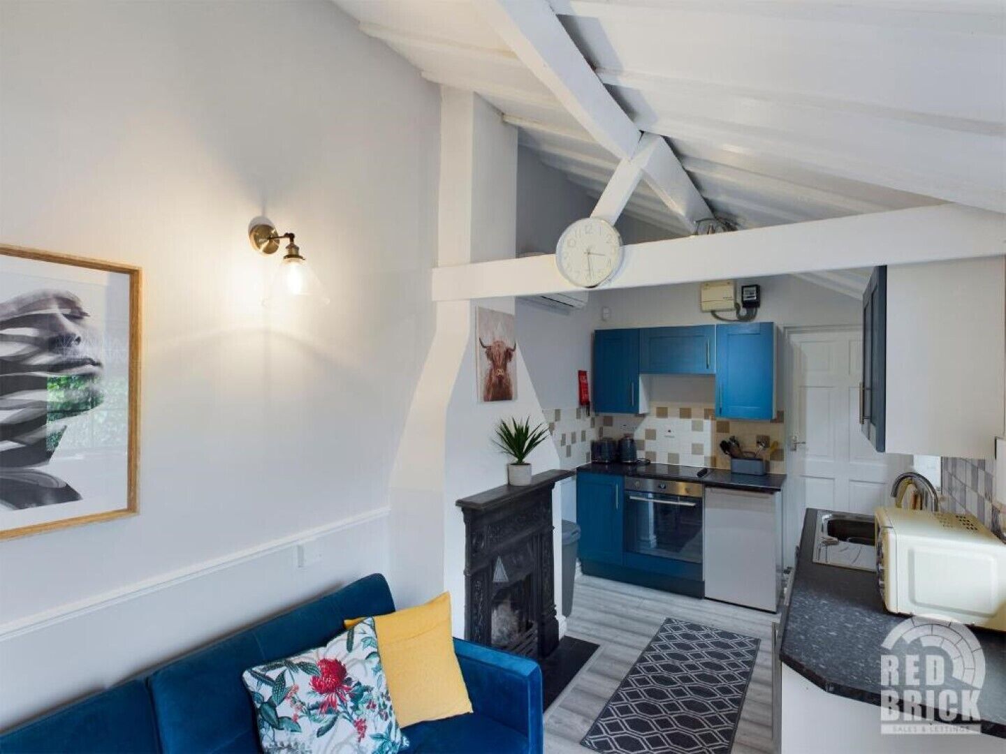 A modern living room with a blue sofa, a fireplace, and a kitchen in the background.