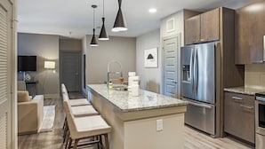 A modern kitchen with a stainless steel refrigerator, granite countertops, and a bar area with bar stools. - Landing | Stylish 2BD, Clubhouse, Courtyard (Austin)