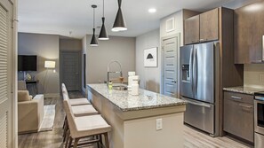 A modern kitchen with a stainless steel refrigerator, granite countertops, and a bar area with bar stools.