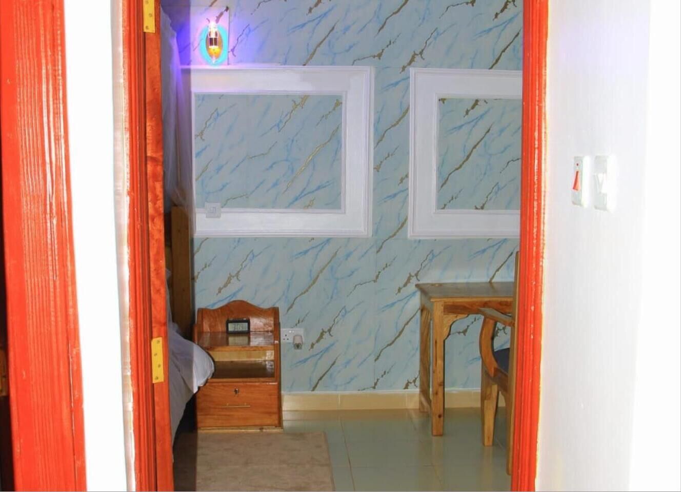 A room with a bed, a wooden nightstand, a small table, and a wall-mounted shelf.
