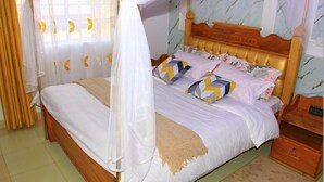 Quarto com cama de dossel, cabeceira de madeira e mesa de cabeceira com relógio.