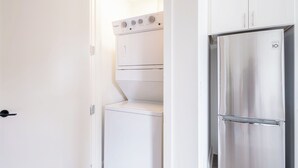 Ein kleiner Waschraum mit einer Edelstahl-Waschmaschine und einem Trockner, einer weißen Tür und einer weißen Wand.