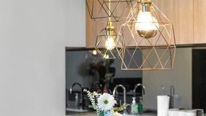 A modern kitchen with a central island, pendant lights, and a vase with flowers. - Modern & Stylish 2BR Apt - CBD - Free Parking (Adelaide)