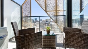 A balcony with wicker furniture, a potted plant, and a view of a cityscape.