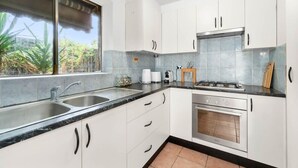 Une cuisine moderne avec des meubles blancs, un plan de travail noir, un évier, une cuisinière et une fenêtre donnant sur un paysage verdoyant.