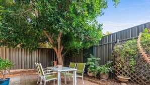 Une terrasse avec une table et des chaises, entourée de plantes en pot et d’un arbre.