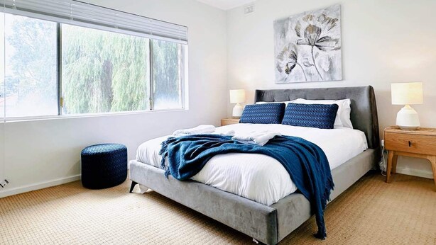 Une chambre moderne avec un grand lit, deux tables de chevet, un ventilateur de plafond et une fenêtre avec des stores.