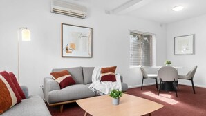 Un salon moderne avec un canapé gris, une table basse en bois et un coin repas avec des chaises blanches.