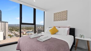 Quarto de hotel com uma cama grande, vista da cidade e uma pequena mesa de cabeceira.