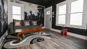 A living room with a grey sofa, a wooden coffee table, and a black and white rug. There are two windows with white frames and a door with a 'No Entry' sign. - Cleveland’s Legends' Lair | Themed | Sleeps 4 (Cleveland)