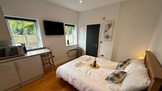 A bedroom with a bed, bedside table, and a TV mounted on the wall. - Romantic King Bed Countryside Couples Cabin (Salisbury)