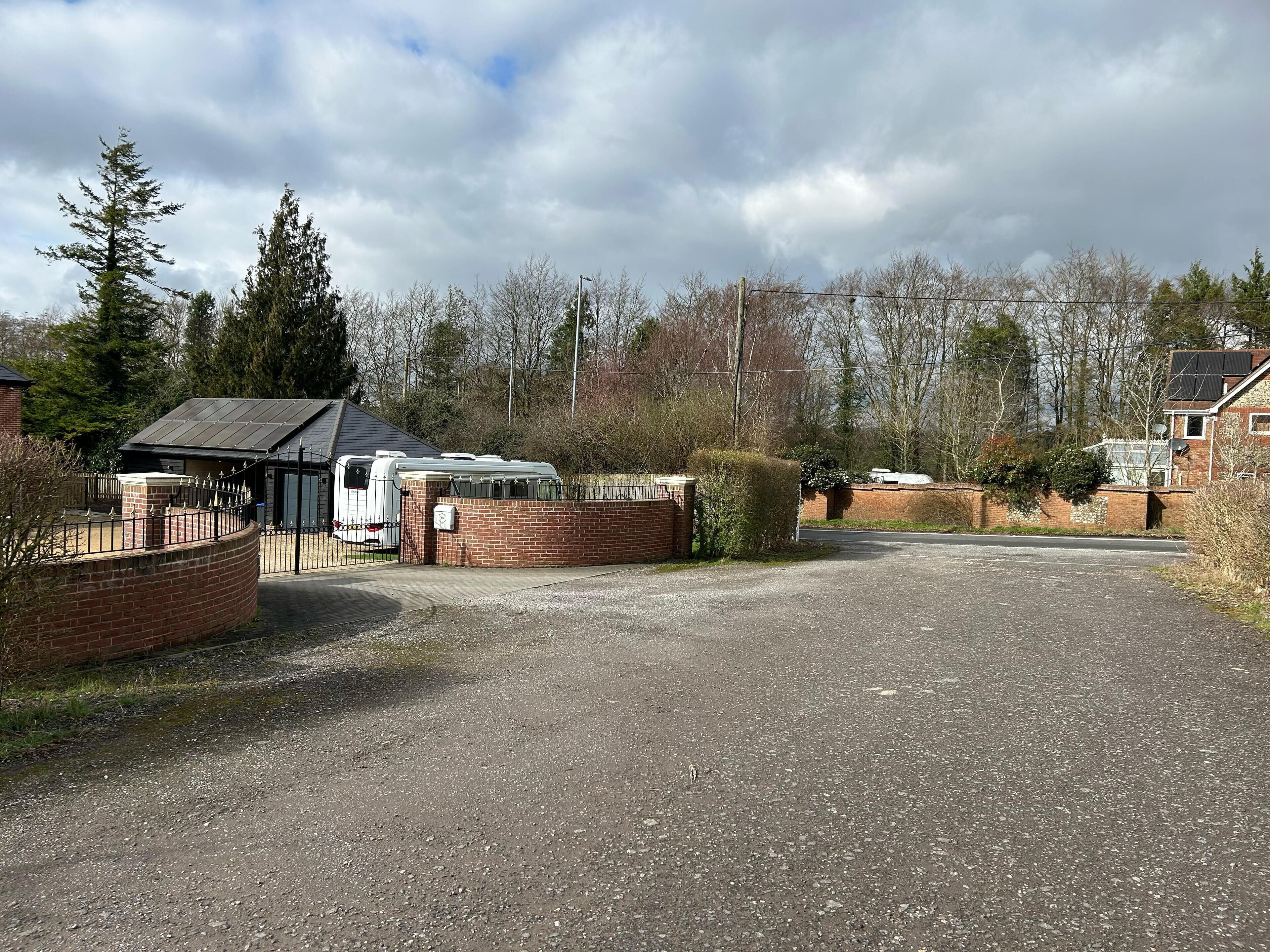 Een parkeerplaats met grind, een caravan en een bakstenen gebouw.