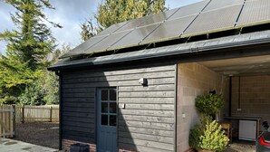 A small building with a dark wooden exterior, a blue door, and a garage with a car parked inside. - Romantic King Bed Countryside Couples Cabin (Salisbury)