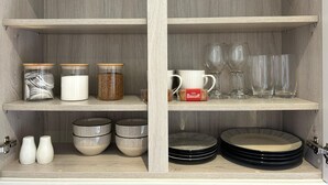 A wooden cabinet with three shelves. The top shelf holds three glass jars with lids, the middle shelf has a white mug and a pack of Biscuits, and the bottom shelf contains several black and white patterned bowls and two white salt shakers. - Romantic King Bed Countryside Couples Cabin (Salisbury)