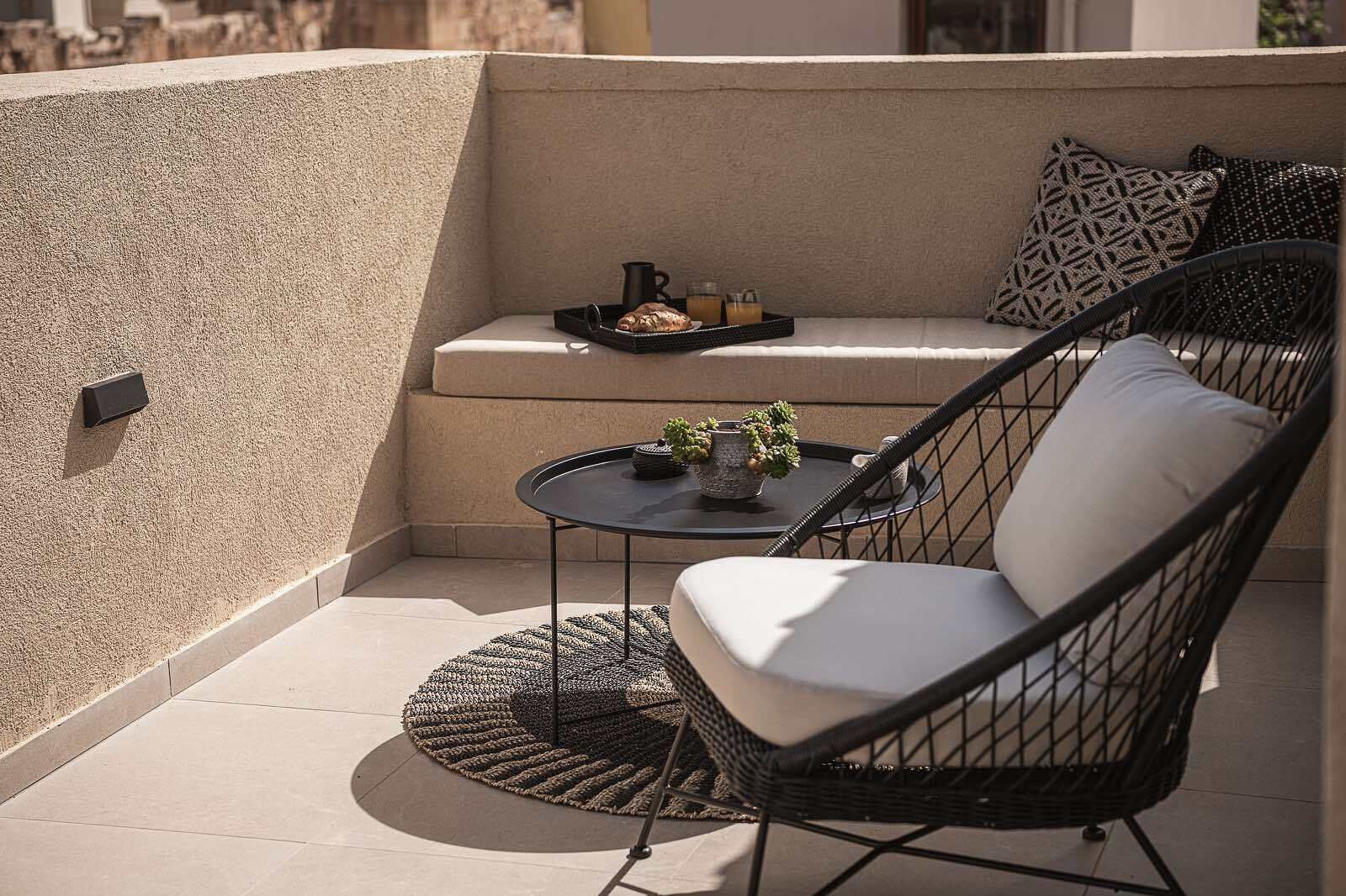 A balcony with a cushioned chair, a small round table, and a tray with food and drinks.