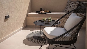 A balcony with a cushioned chair, a small round table, and a tray with food and drinks. - Copal Simple Staying (Chania)