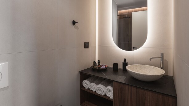 Un bany modern amb un mirall oval gran, un lavabo independent i tovalloles ordenadament arremolinades a una estant.