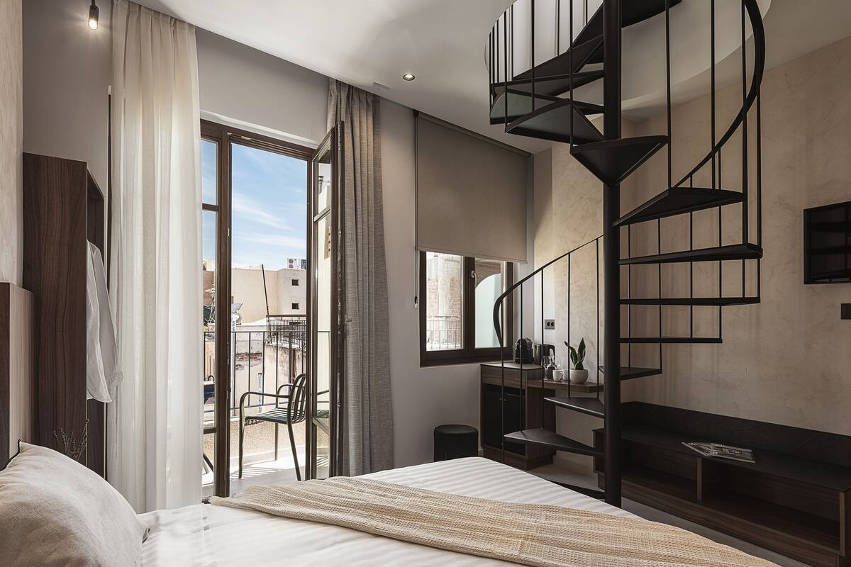 A modern bedroom with a bed, a large window, a spiral staircase, and a balcony.