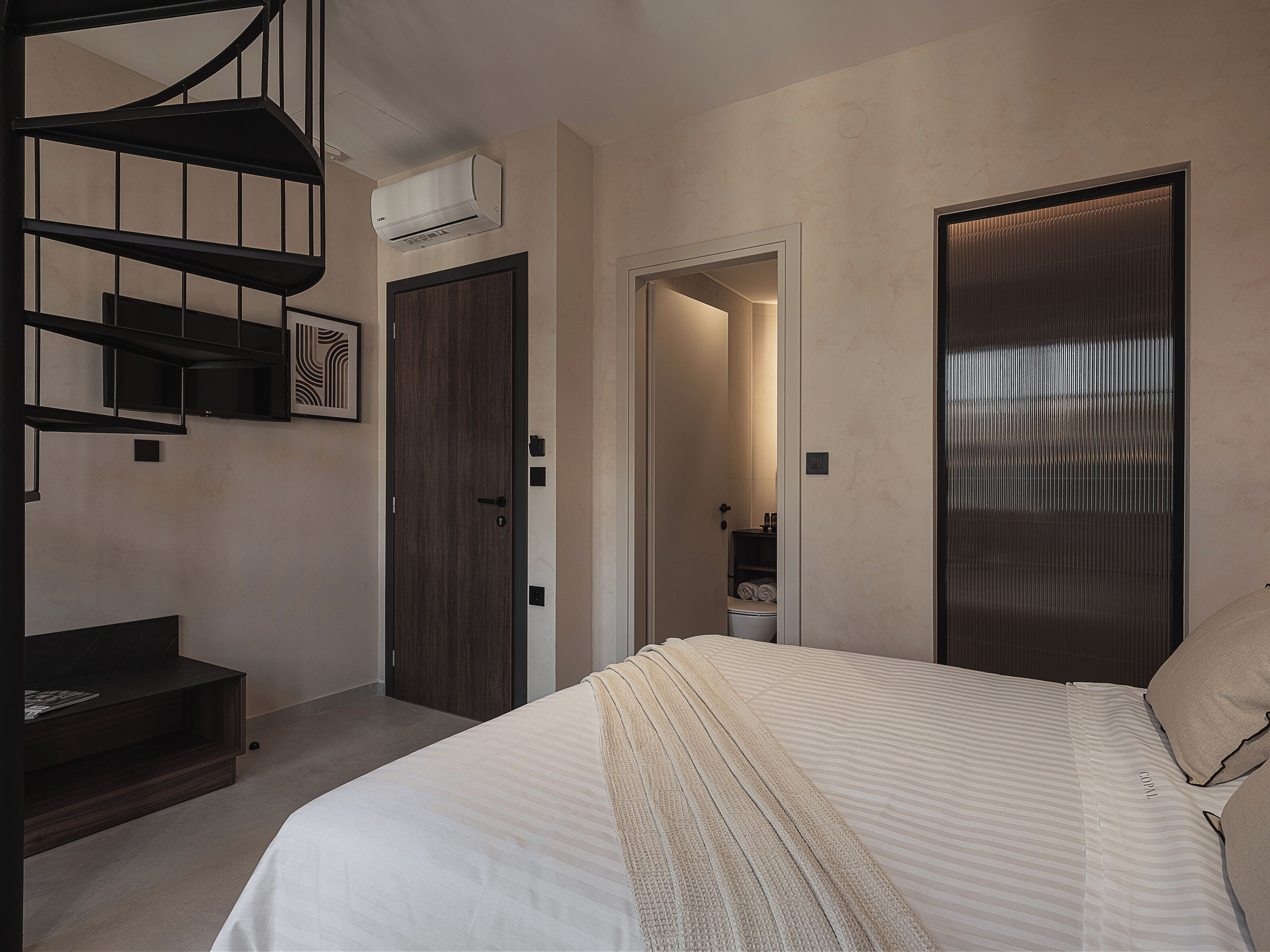 A modern bedroom with a bed, a built-in wardrobe, a staircase, and a bathroom visible through an open door.