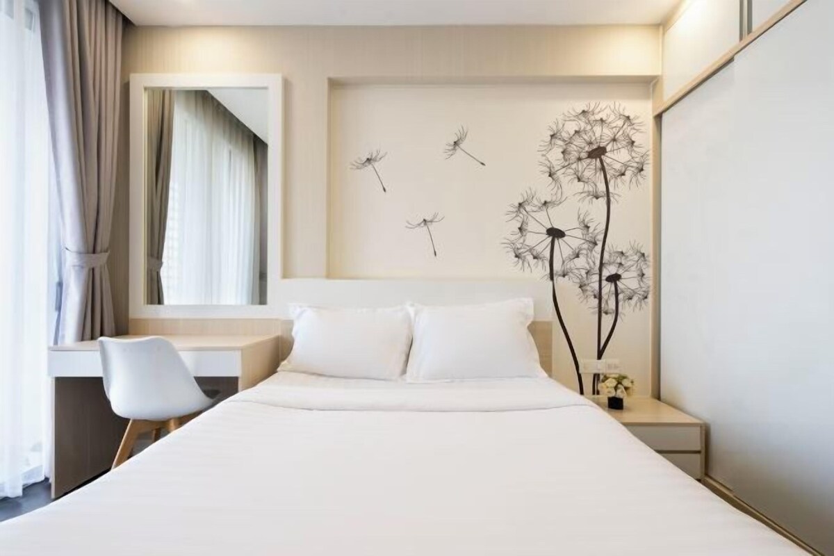 Une chambre d’hôtel avec un grand lit, un bureau et une chaise. Un tableau représentant des pissenlits est accroché au mur.