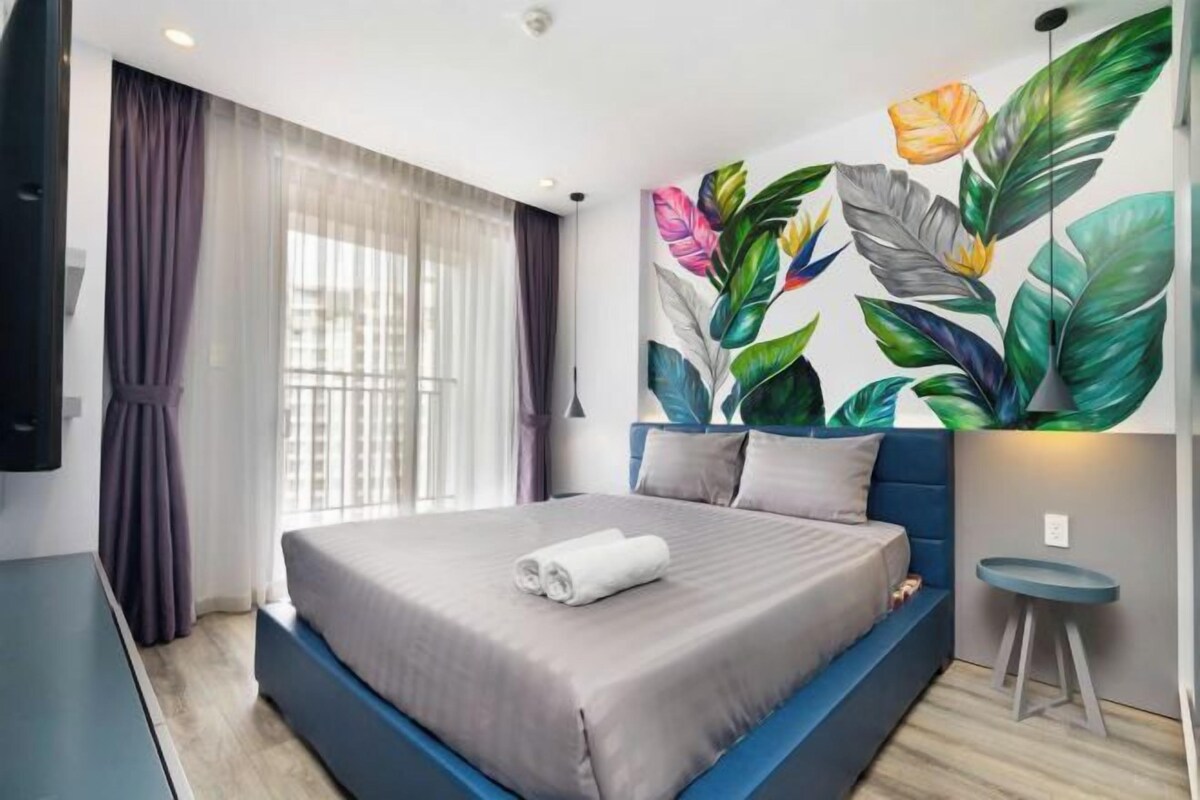 Quarto de hotel moderno com uma cama grande, vista para a cidade e um mural colorido na parede.