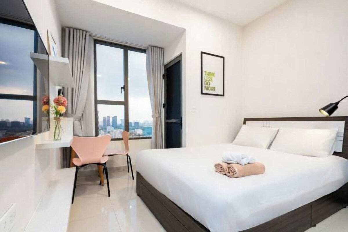 Une chambre d’hôtel moderne, dotée d’un grand lit, d’un bureau, d’une chaise et offrant une vue sur la ville par la fenêtre.