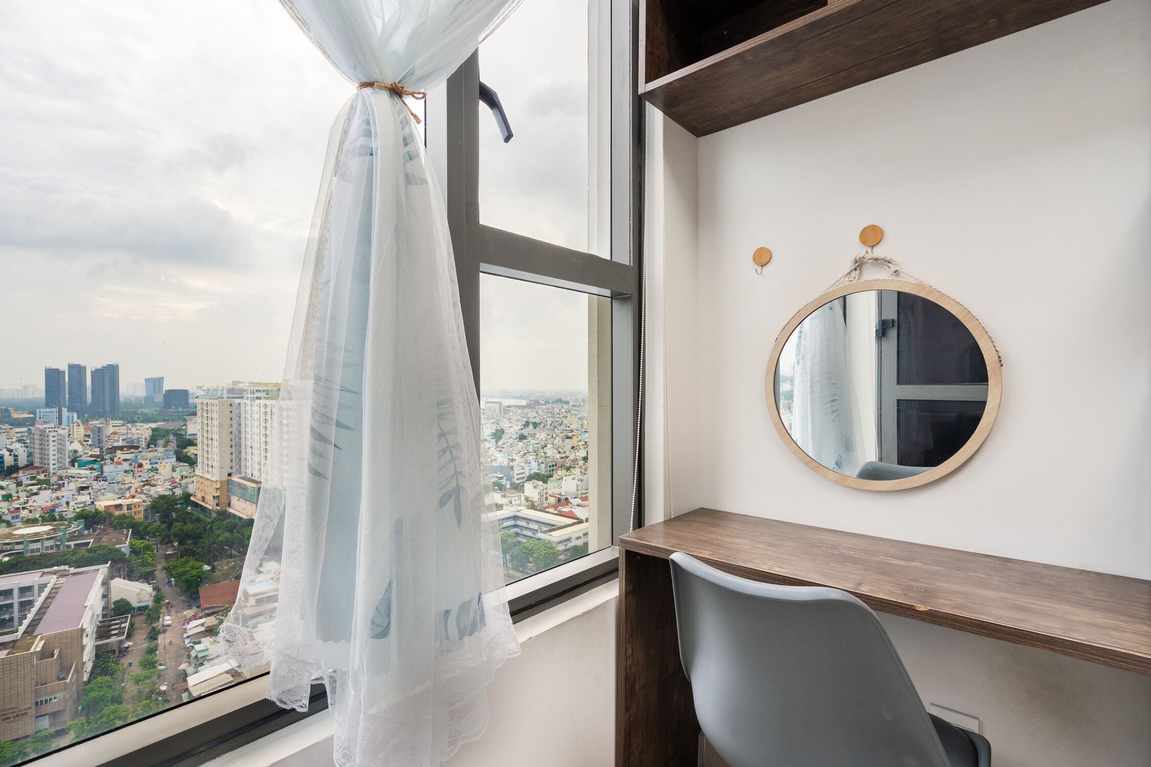 A room with a large window, a round mirror, and a desk.