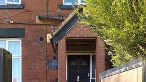Un bâtiment en briques avec une porte noire, un petit seuil menant à l’entrée et un portail en métal.
