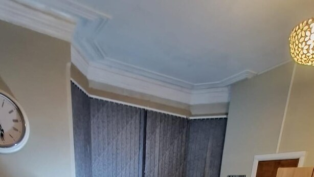 Une chambre à coucher avec un lit en bois, un canapé gris, une armoire et une horloge au mur.