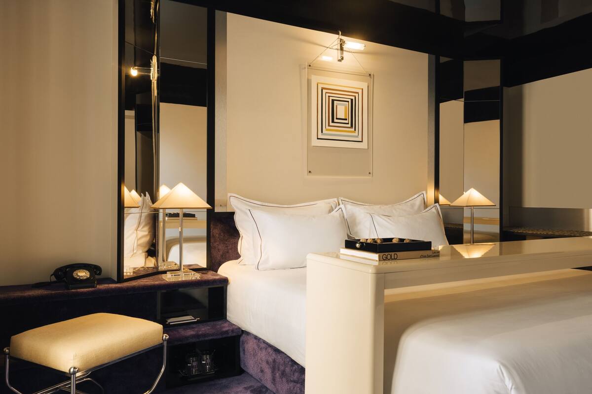 A hotel room with a large bed, bedside tables, a mirror, and a wall art piece.
