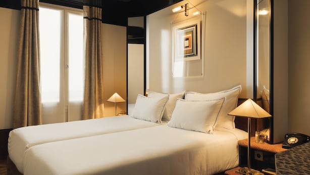 A hotel room with two beds, a nightstand with a lamp, a mirror, and a framed picture on the wall.