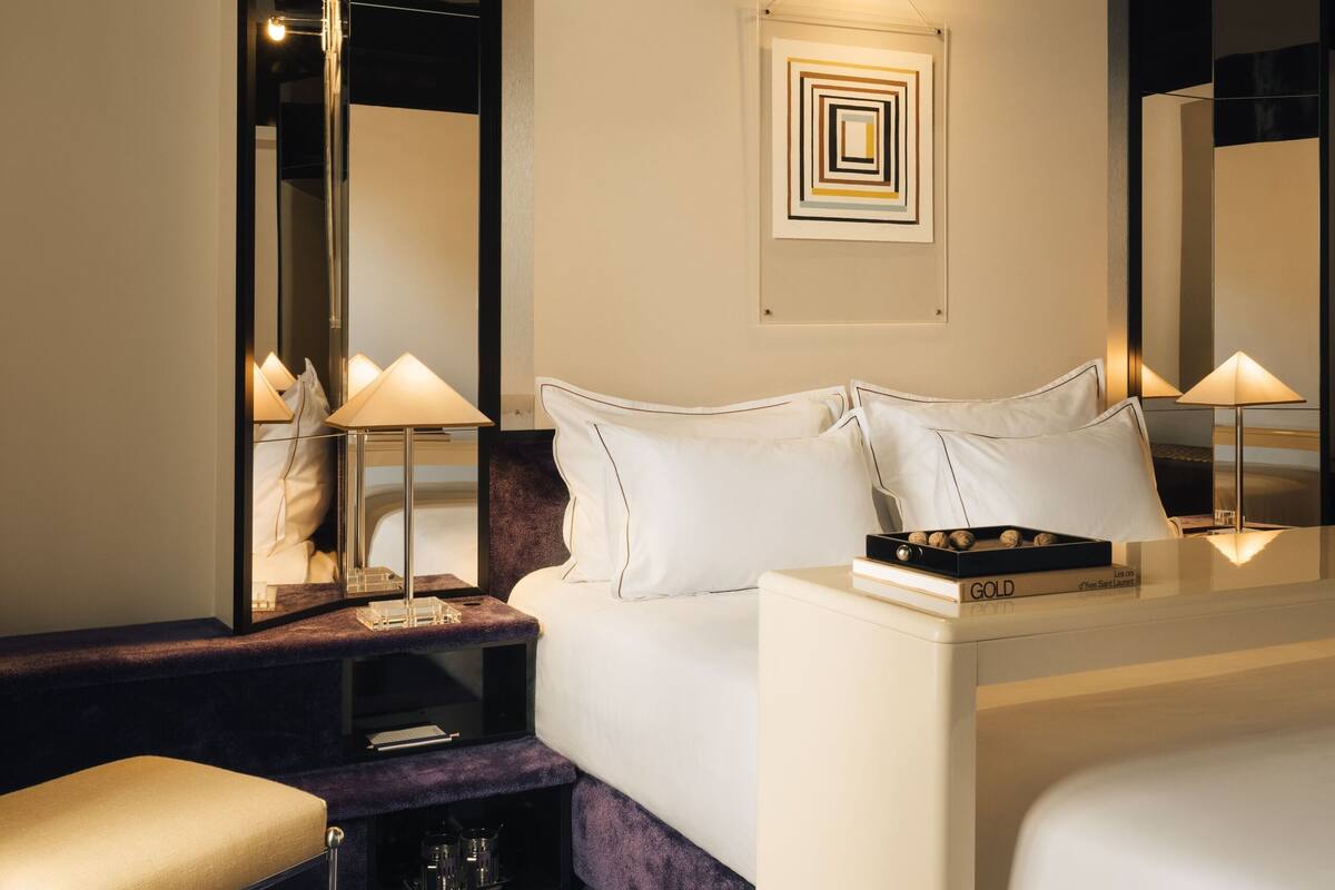A modern hotel room with a large bed, a bedside table, a chair, and a mirror.