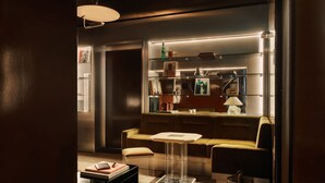 A modern living room with a sofa, a small table, and a kitchen area with shelves and appliances.