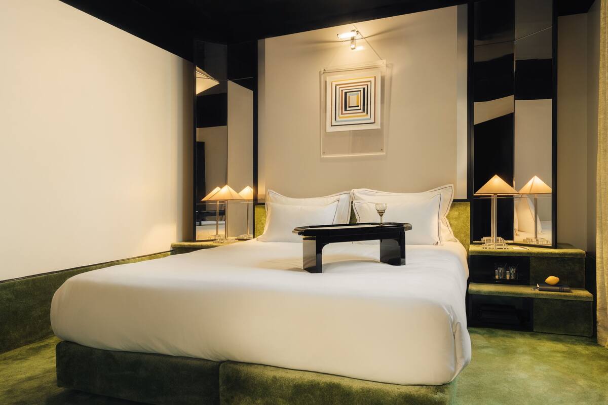 A neatly made bed with white linens, a bedside table with a lamp, and a wall-mounted artwork.