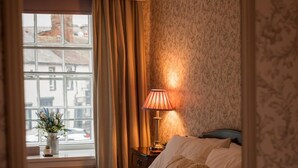 Une chambre à coucher avec un lit, une table de chevet, une lampe et une fenêtre avec des rideaux.