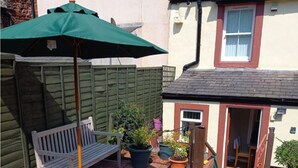 Une terrasse avec une table préparée pour prendre des boissons, un banc et un parasol vert.