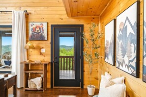 A wooden cabin interior with a door leading to a balcony, a lamp, a framed painting, and a potted plant. - Amazing Mountain View, Hot Tub, Game Room! (Sevierville)