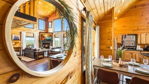 A wooden cabin interior with a dining area, kitchen, and living room, featuring a large circular mirror. - Amazing Mountain View, Hot Tub, Game Room! (Sevierville)