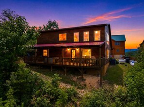 A wooden cabin with a deck, multiple windows, and a visible outdoor area. - Amazing Mountain View, Hot Tub, Game Room! (Sevierville)