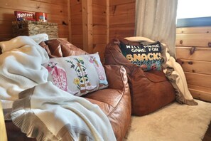 A cozy cabin interior with a brown leather couch, a white blanket, and a pillow with a floral design. - Amazing Mountain View, Hot Tub, Game Room! (Sevierville)